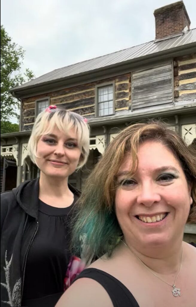 a selfie of Becky and Diana, co-hosts of the Homespun Haints podcast, smiling in front of the historic Exchange Place in Kingsport, TN, a key destination on their paranormal Appalachian road trip, with the rustic, stone facade of the building providing a timeless, somber backdrop.