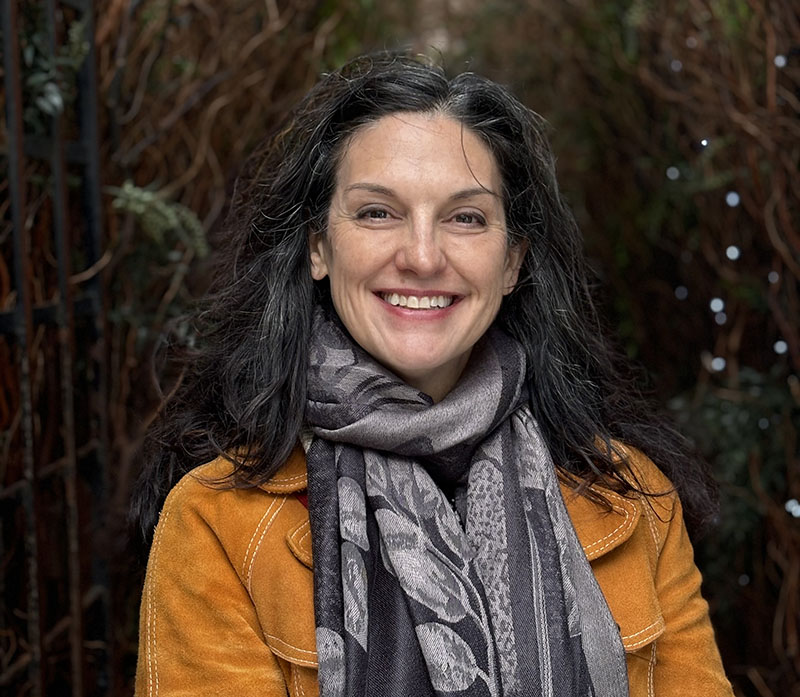 Artist and author Stacey Williams-Ng smiling out from a thicket in Scotland. 