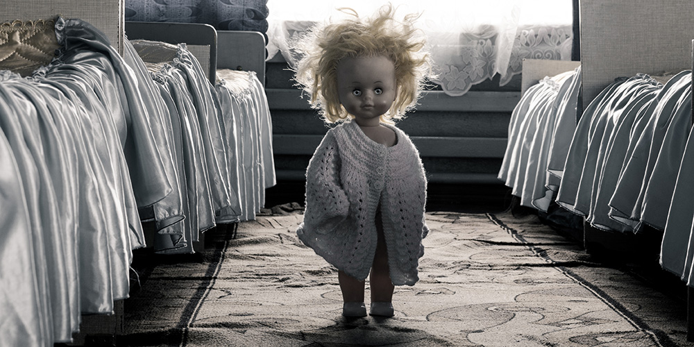 creepy inspirited doll standing between two beds