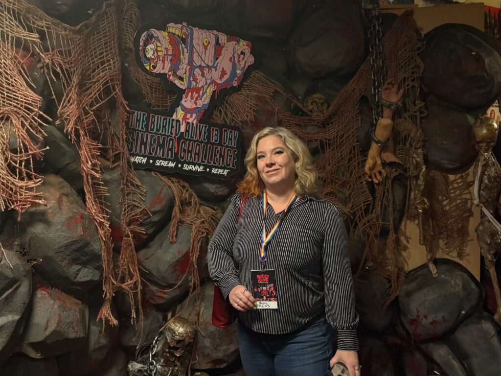 A stunningly gorgeous woman stands in front of the intentionally disturbing sign for Buried alive horror film festival