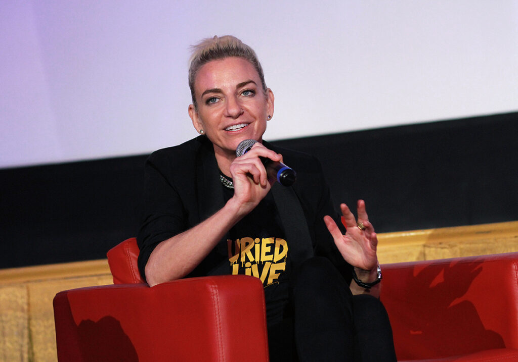 Queens of the Dead director Tina Romero on stage at buried Alive film fest Atlanta, speaking animatedly into a microphone