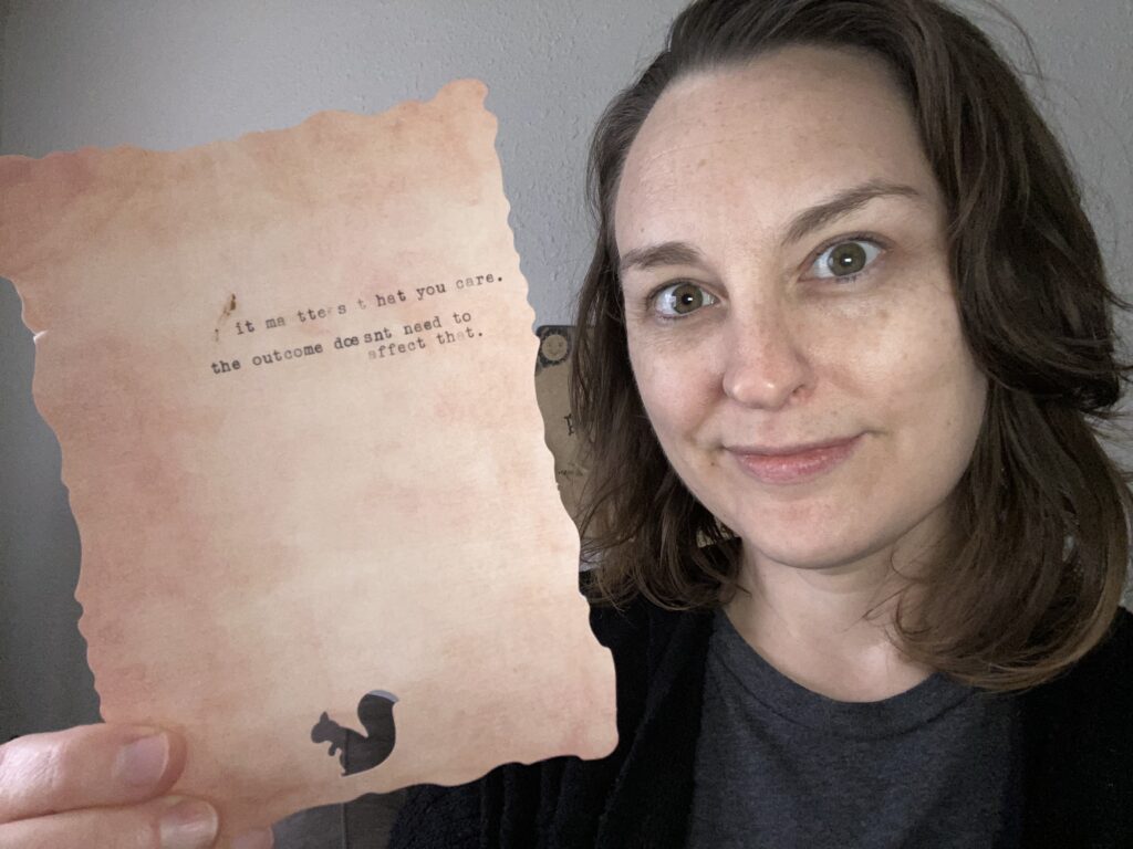 An untouched headshot of the host, Diana, smiling and holding up an artsy peach-colored piece of paper with a squirrel cut-out and this mantra, typed inexpertly on a vintage typewriter: it matters that you care. the outcome doesn't need to affect that. She created this at the Galentine's day event at the Kismet Collective office, which didn't seem very haunted during the event.